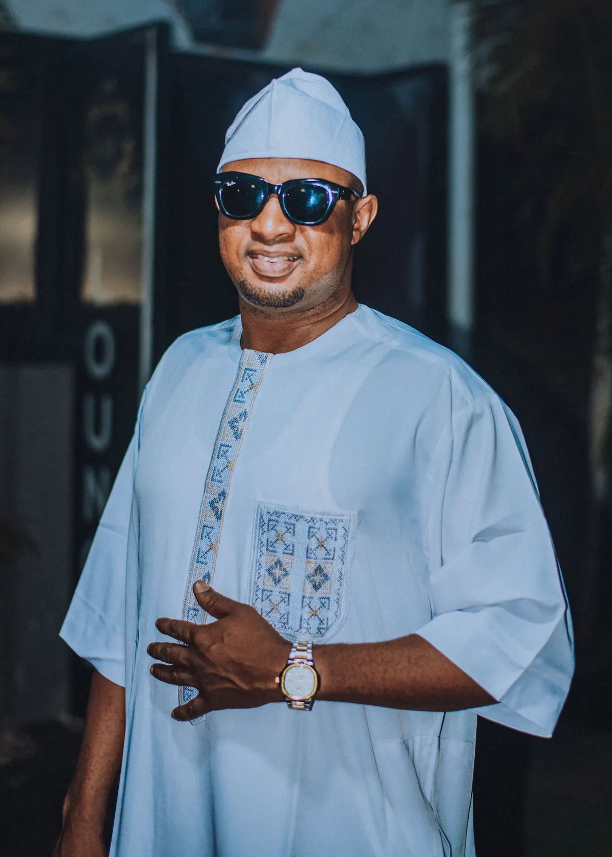 A man in a white embroidered kaftan, cap and sunglasses smiles at the awards night