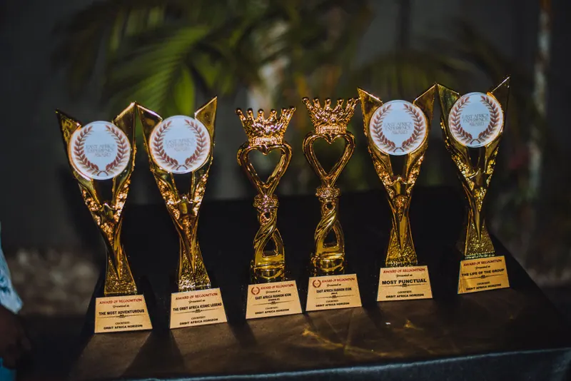 Six gold trophies lined up on a table, each with an East Africa Experience Award plaque