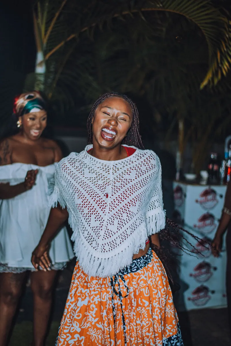 A woman in a white crochet top and orange skirt laughs with her eyes shut on her way to the front
