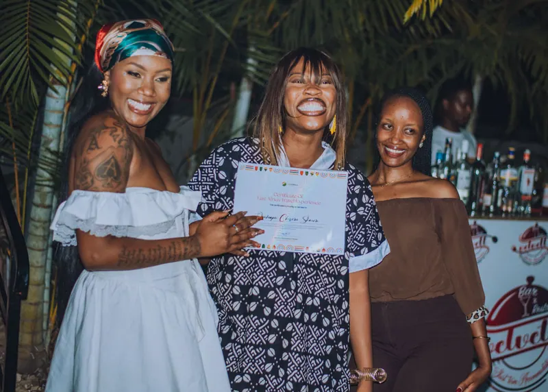 A woman in a black and white print dress laughs as she is handed her certificate