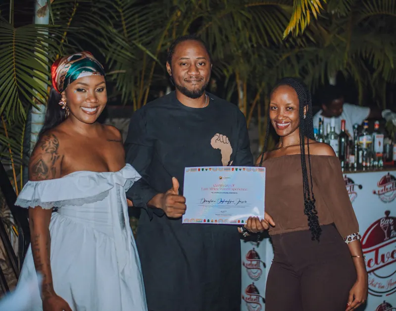 A man in a black outfit gives a thumbs up with his certificate