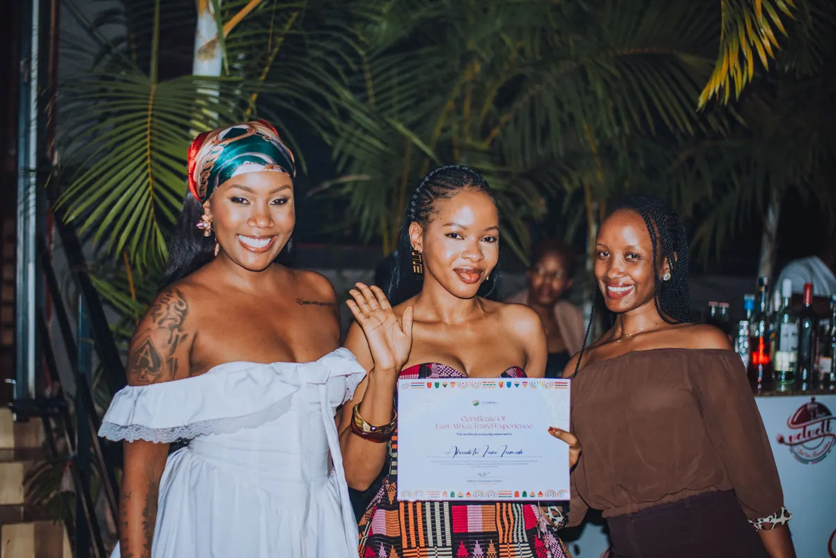 A woman in a kente-pattern dress strikes a pose with her certificate