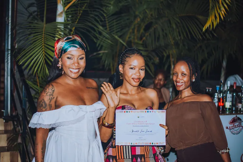 A woman in a kente-pattern dress strikes a pose with her certificate