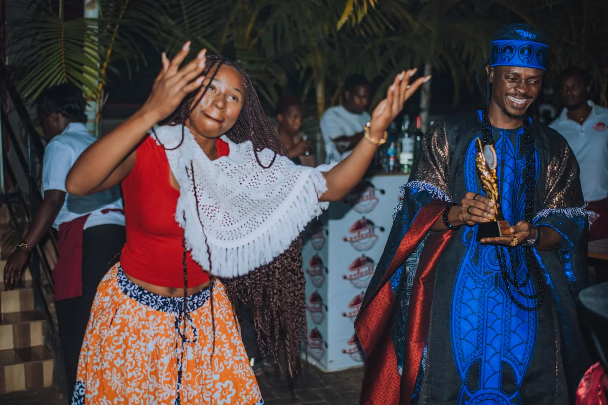 A woman in a white crochet top throws her hands up in shock as her name is called