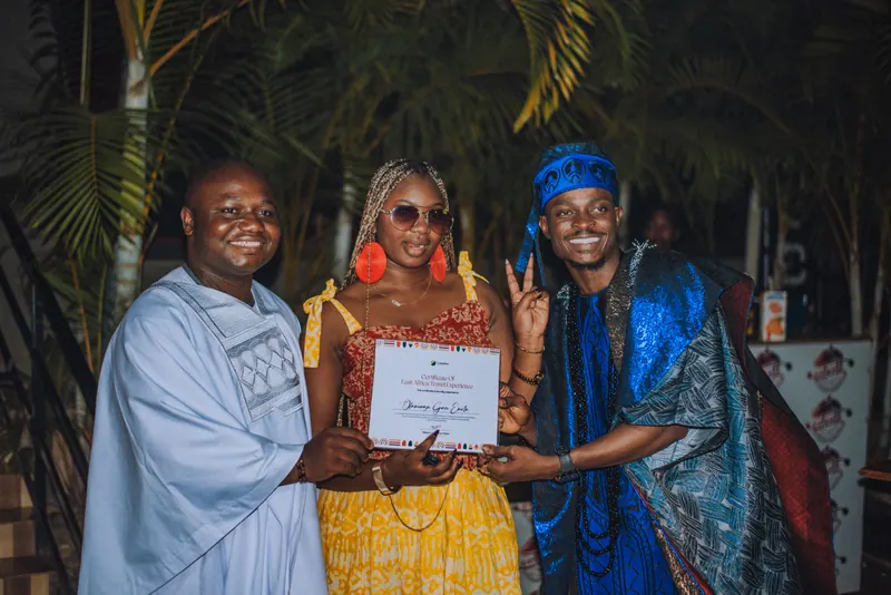 A woman in a yellow adire kimono receives her certificate from the two men presenting