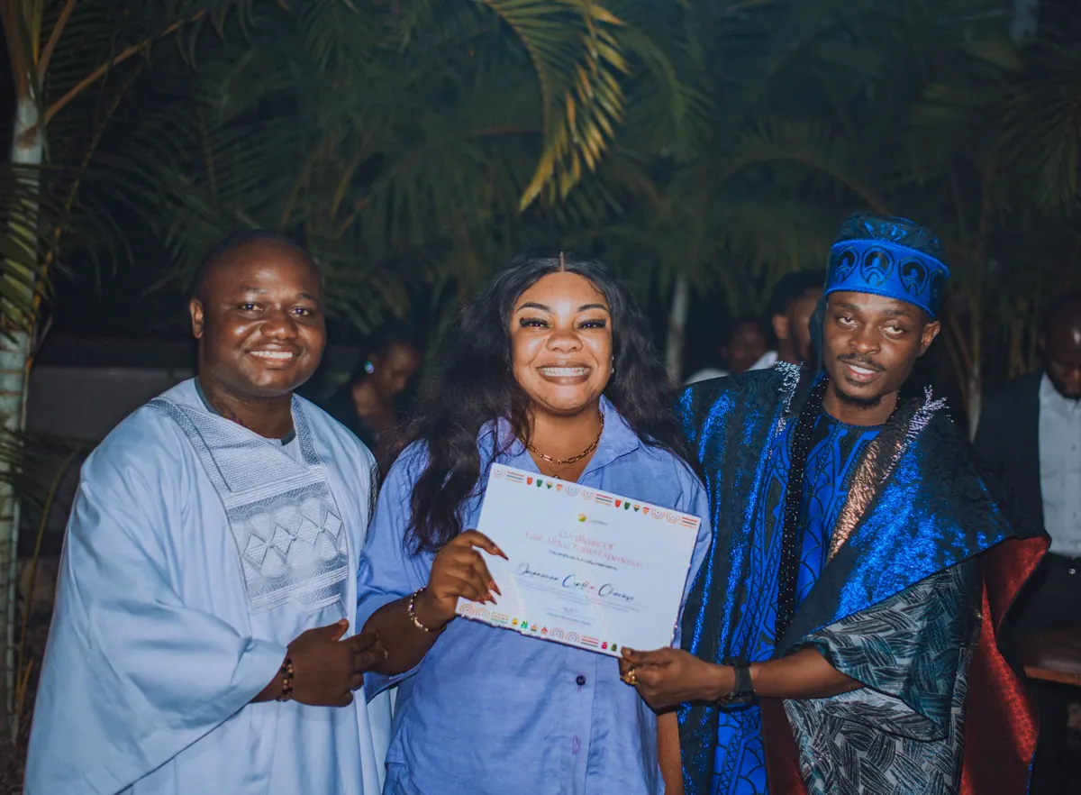 A woman in a pale blue shirt dress holds her certificate between the two men presenting