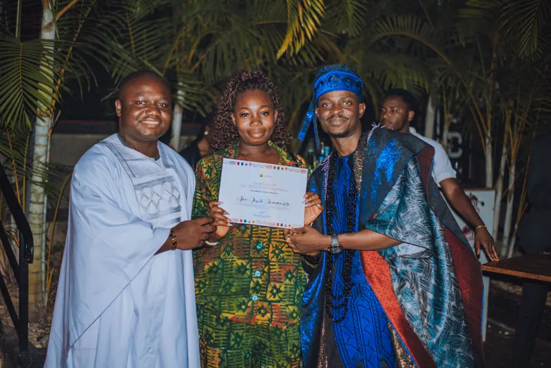 A woman in a green print dress receives her certificate from the two hosts