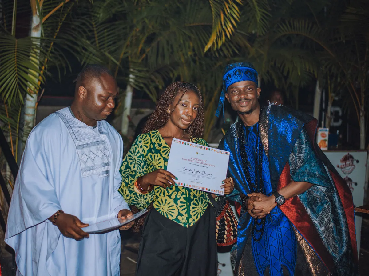 A woman in a green lace top holds up her certificate between the two hosts