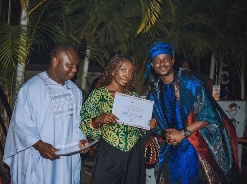 A woman in a green lace top holds up her certificate between the two hosts