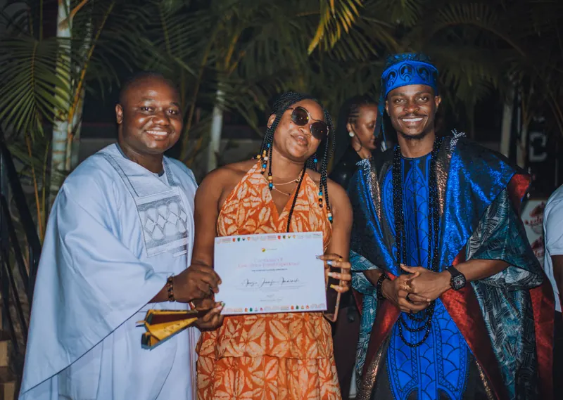 A woman in an orange print dress leans in, smiling, with her certificate