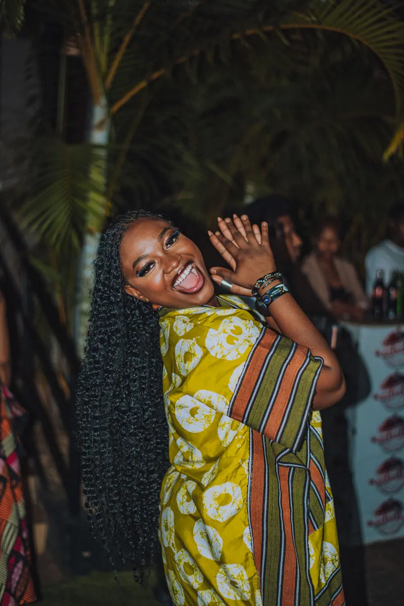 A woman in a yellow and green striped kimono throws her hands up, laughing