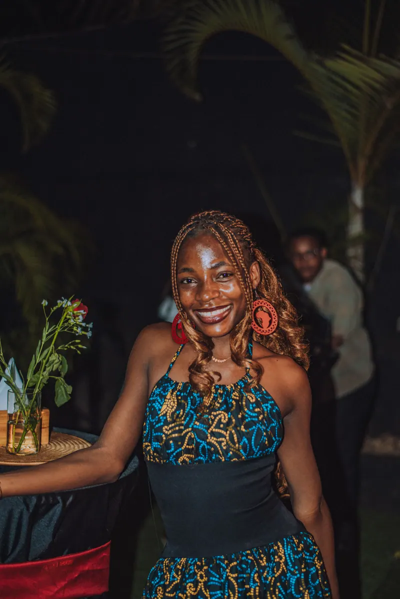 A woman in a teal print dress smiles beside a cocktail table