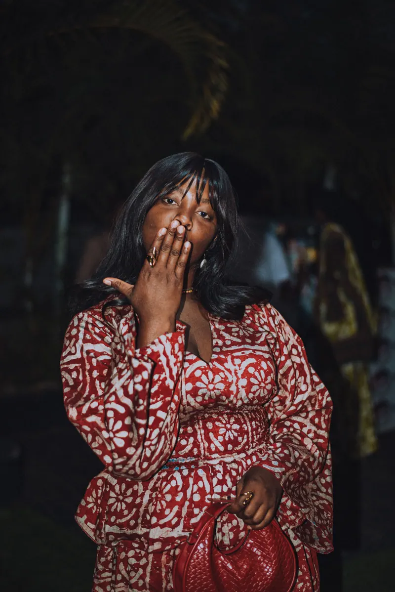 A woman in a red and white adire dress blows a kiss to the camera