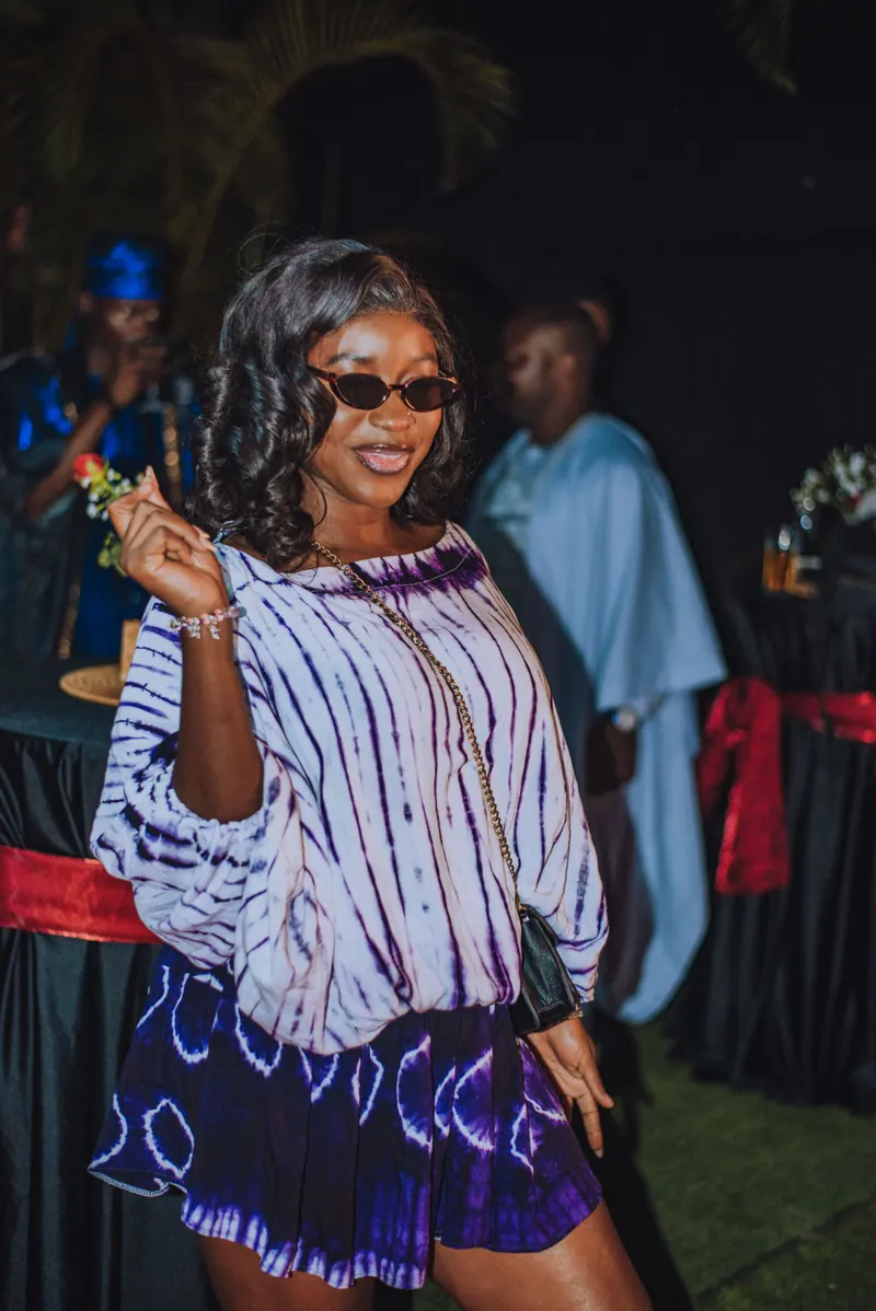 A woman in a purple tie-dye top and skirt dances in sunglasses