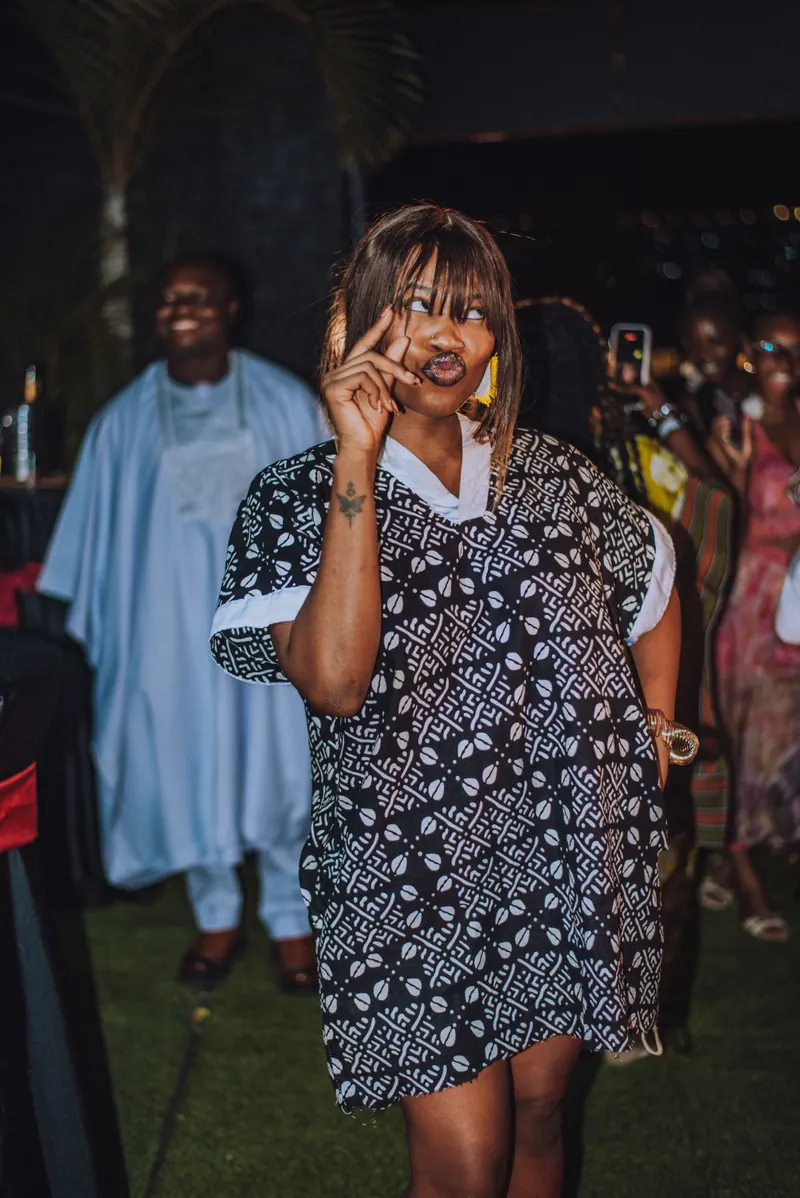 A woman with a fringe in a black and white print dress flashes a peace sign