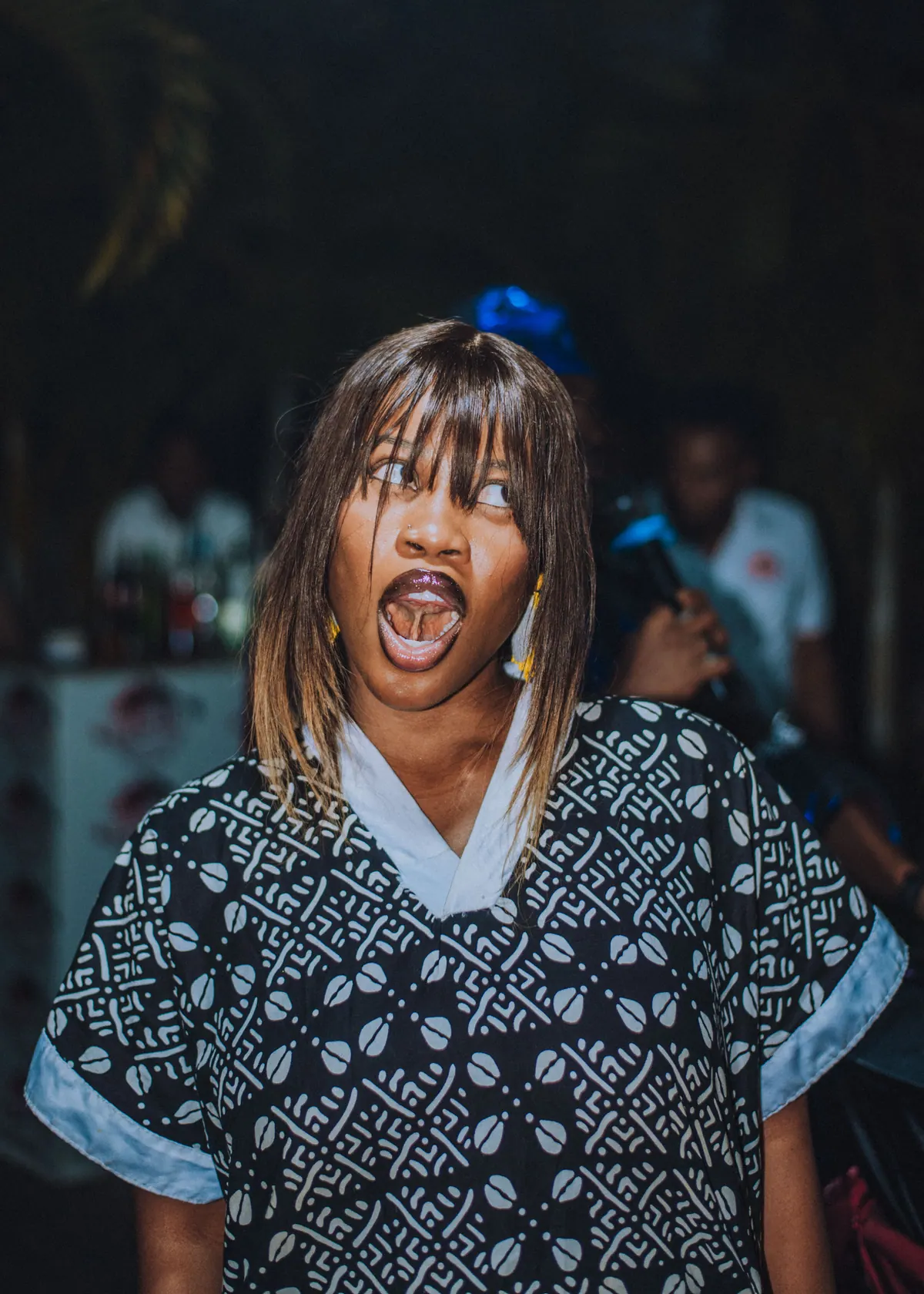A woman in a black and white print dress pulls a wide-mouthed funny face