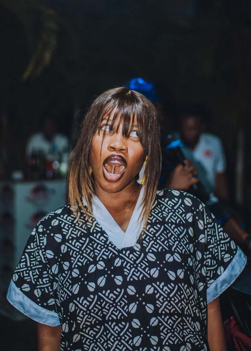 A woman in a black and white print dress pulls a wide-mouthed funny face