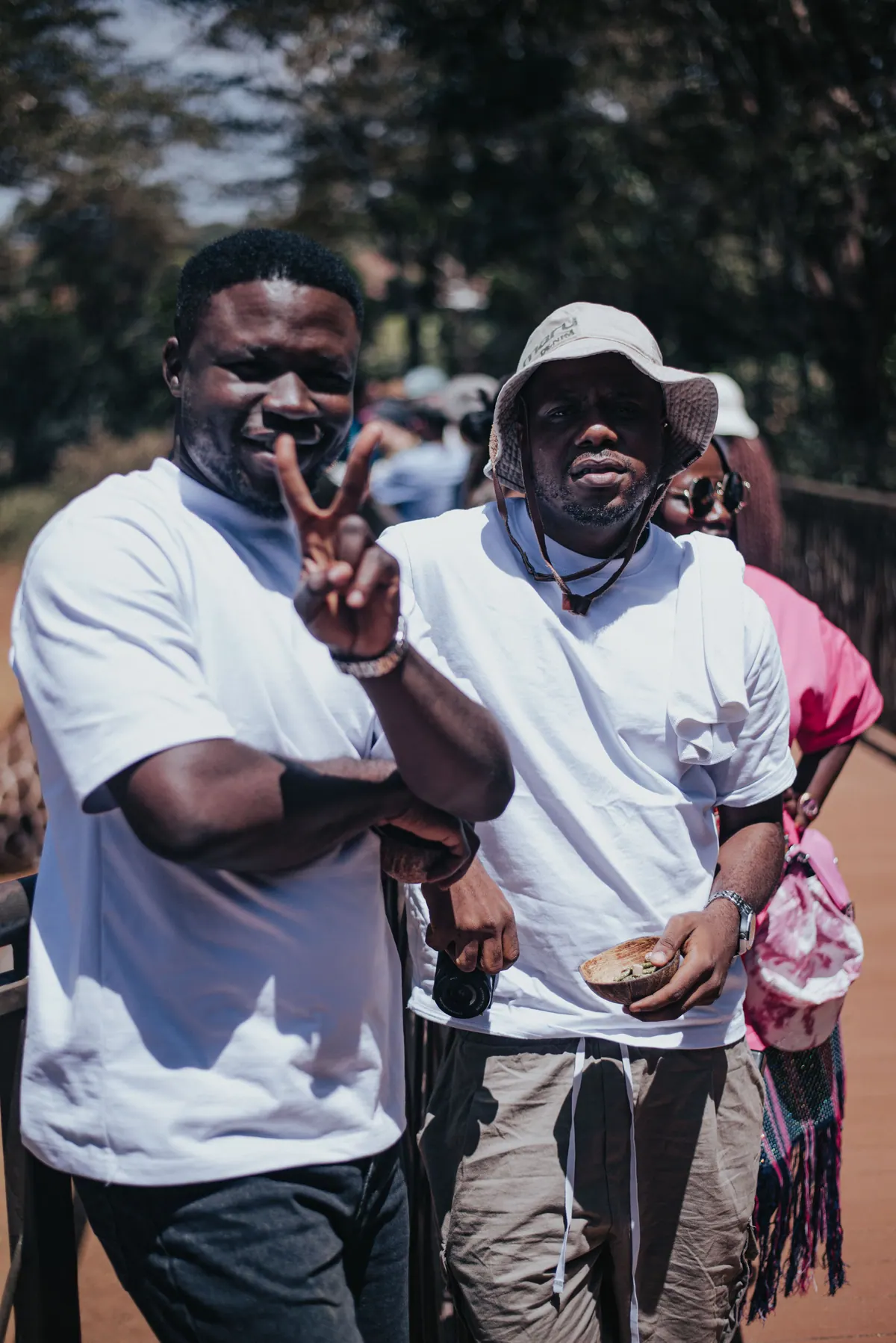 Two men in white T-shirts grin at the camera, one flashing a peace sign
