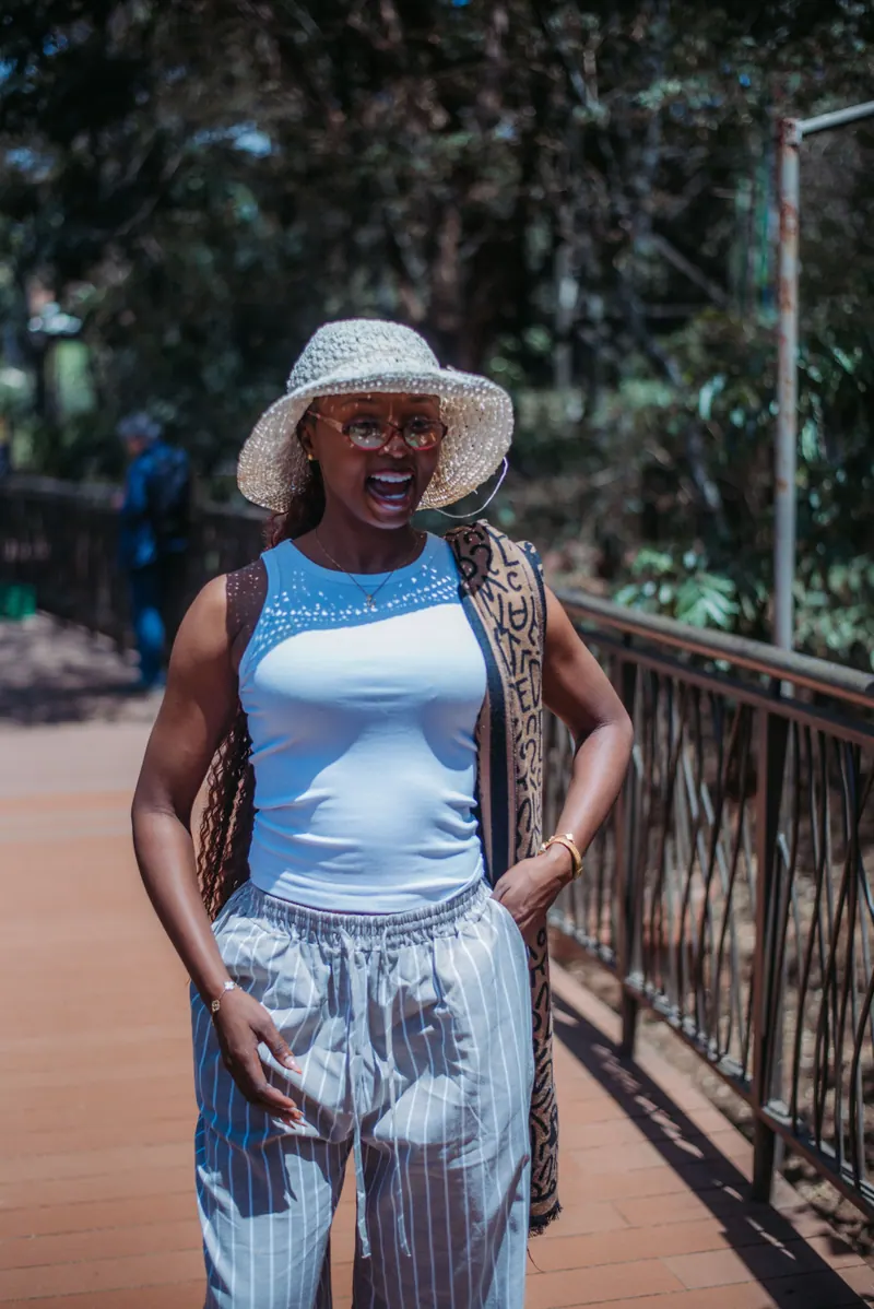 A woman in a crochet hat and striped trousers laughs on the boardwalk at the Giraffe Centre