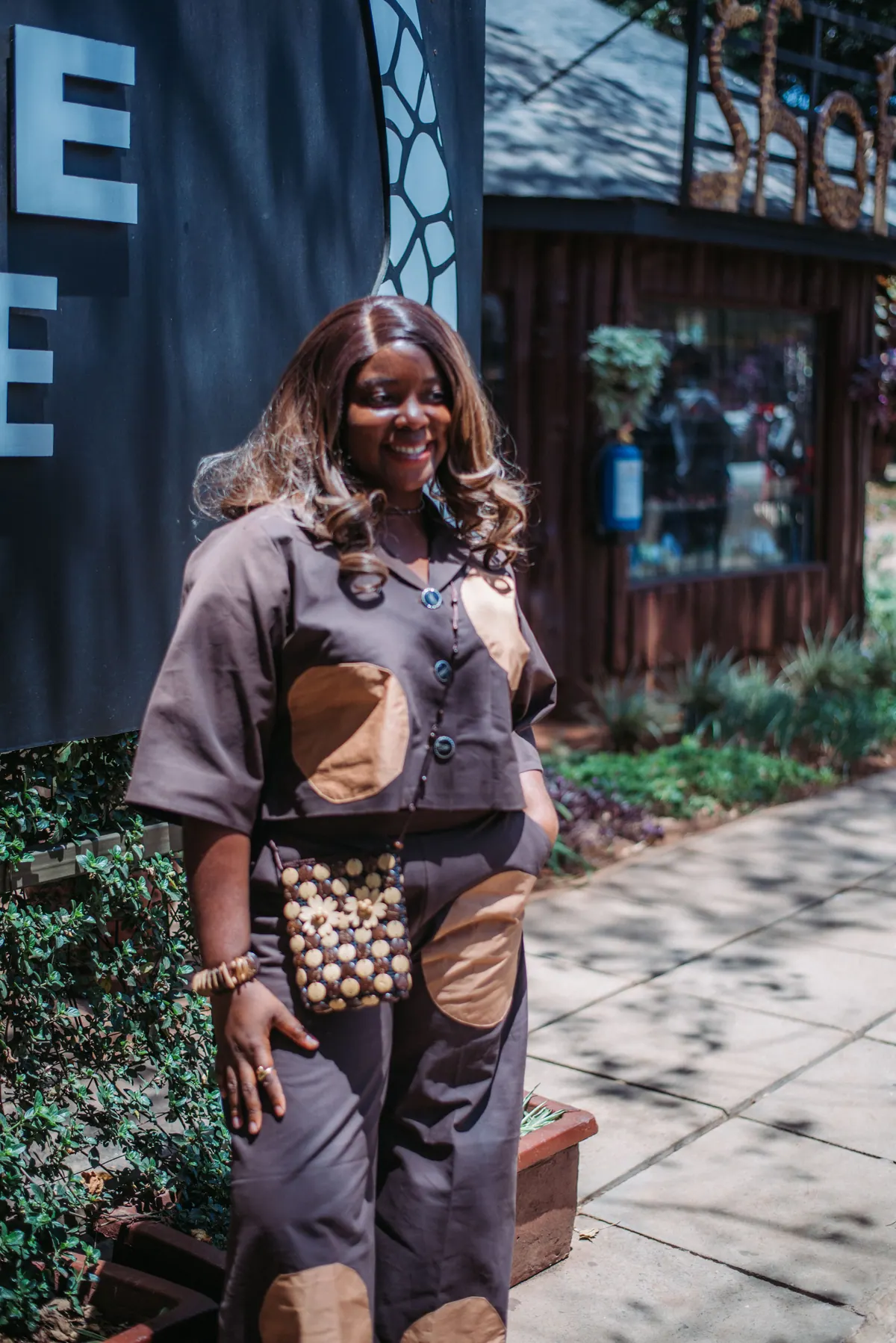 A woman in a brown patchwork outfit walks past the Giraffe Centre sign