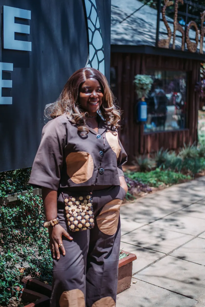 A woman in a brown patchwork outfit walks past the Giraffe Centre sign