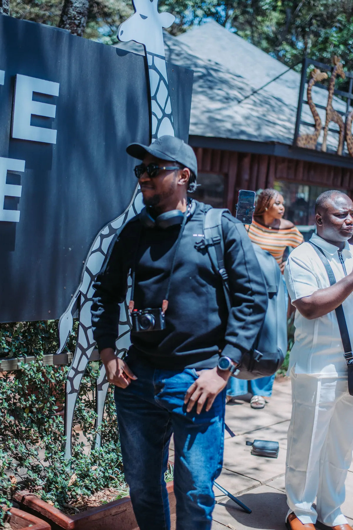 A man in a black jacket and cap smiles outside the Giraffe Centre