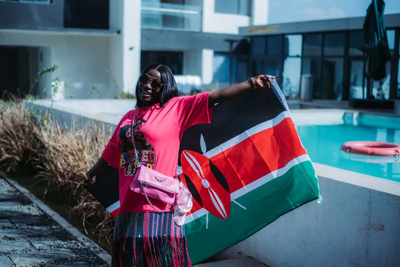 A woman in a pink T-shirt and sunglasses holds a Kenyan flag out beside a hotel pool in Nairobi