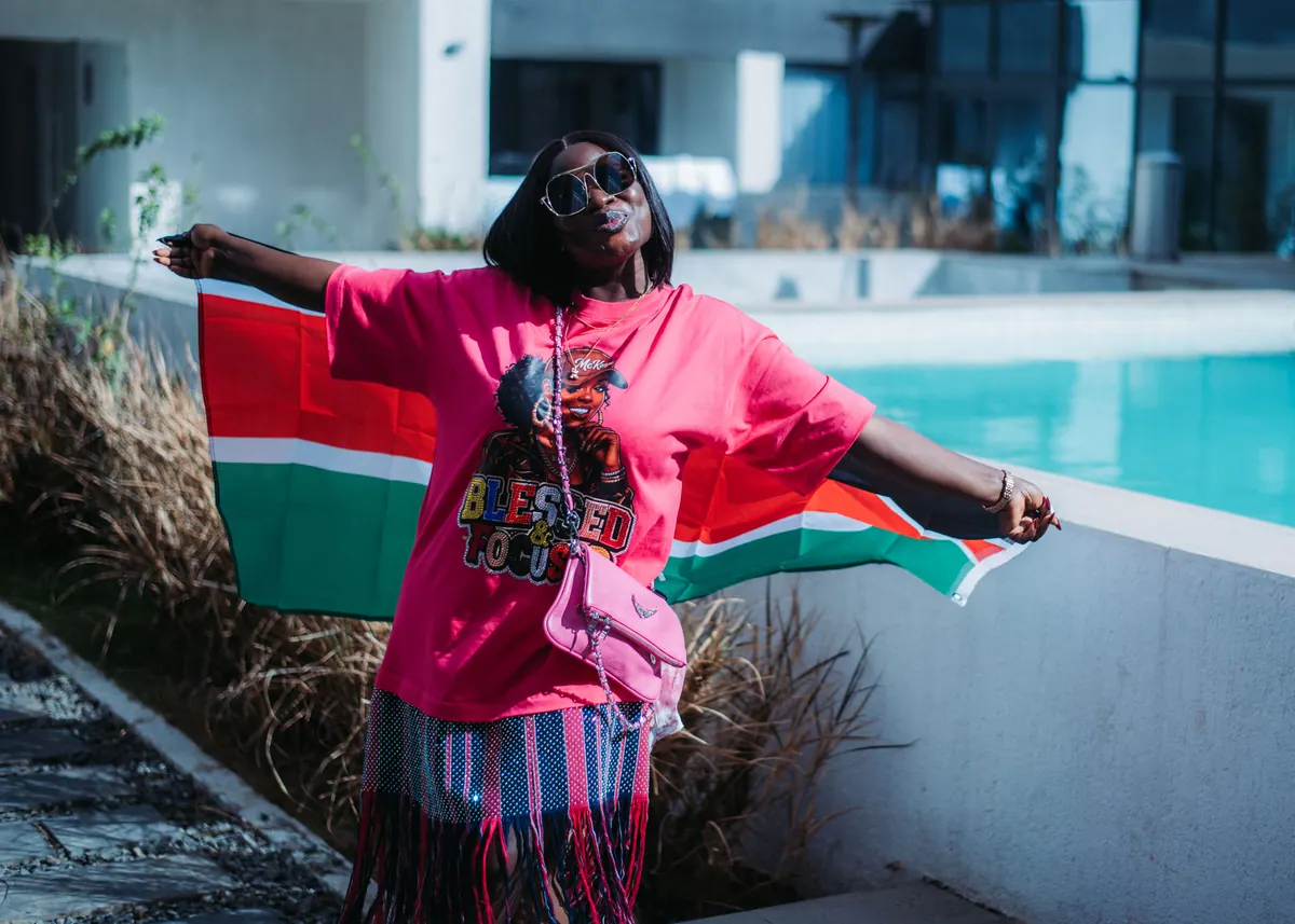 A woman in a pink T-shirt throws her head back with a Kenyan flag stretched out behind her by the pool