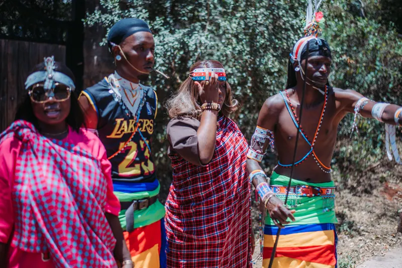 Three of the group in checked shukas pose with a dancer in beads and feathers