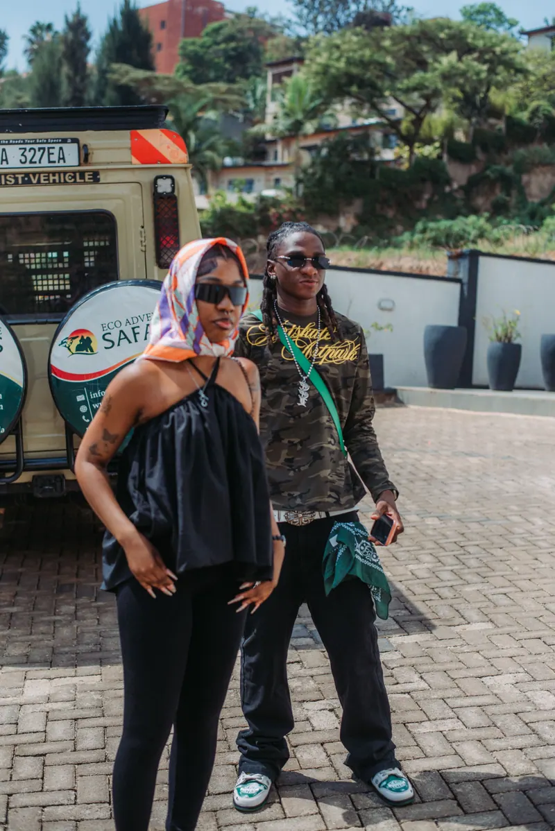 A woman in a headscarf and a man in a camouflage top stand close together in front of a safari vehicle