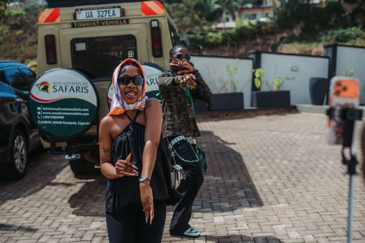 A woman in a headscarf sticks her tongue out mid-dance as a friend poses behind her and a phone films on a tripod