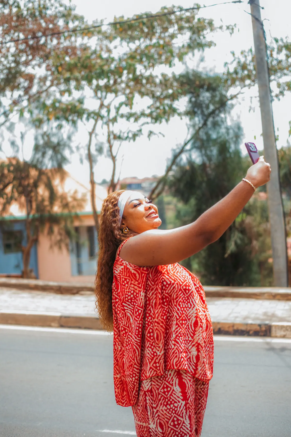 A woman in a red print outfit takes a selfie at the roadside