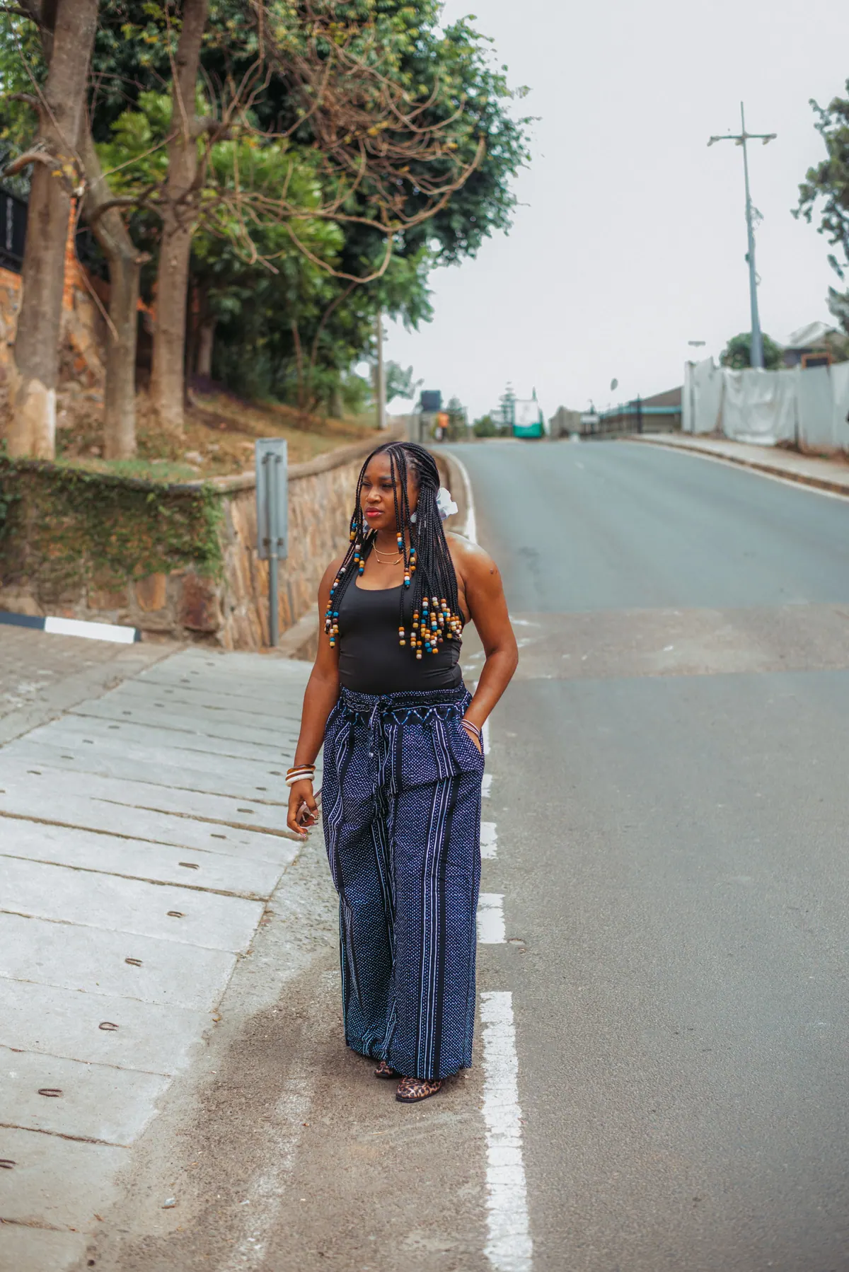 A woman in a black top and wide navy trousers stands in the middle of a quiet road