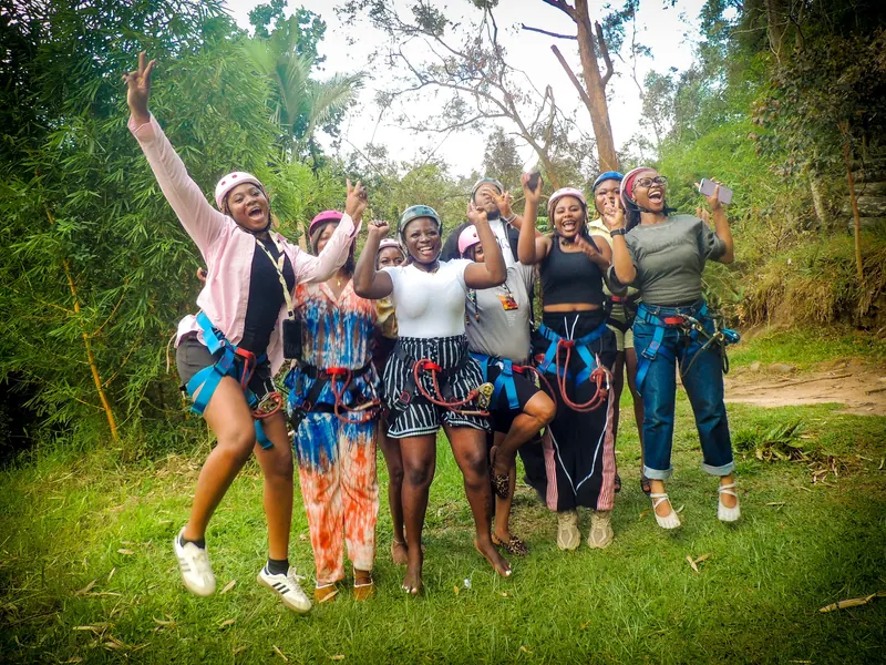 The zip-line crew in harnesses and pink helmets jump and cheer on the grass at Lake Mutanda