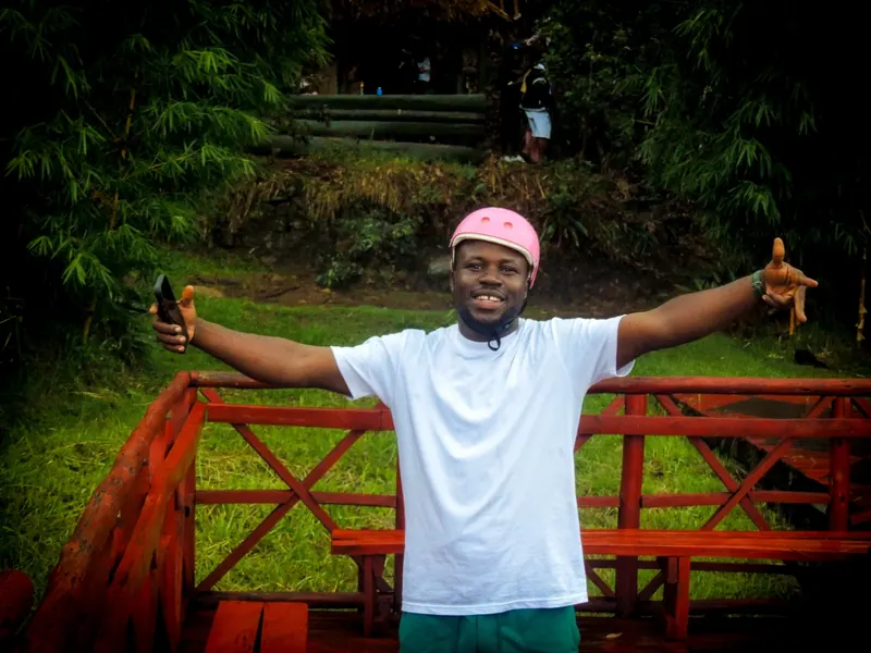 A man in a pink helmet and white T-shirt spreads his arms wide on the landing platform