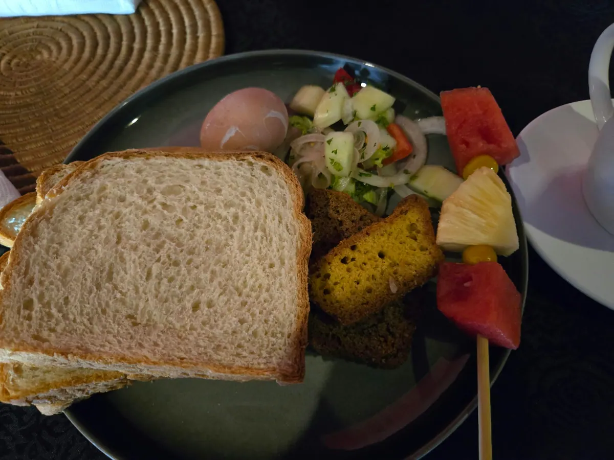 A plate of bread, a boiled egg, salad, cake and a fruit skewer at Velvett