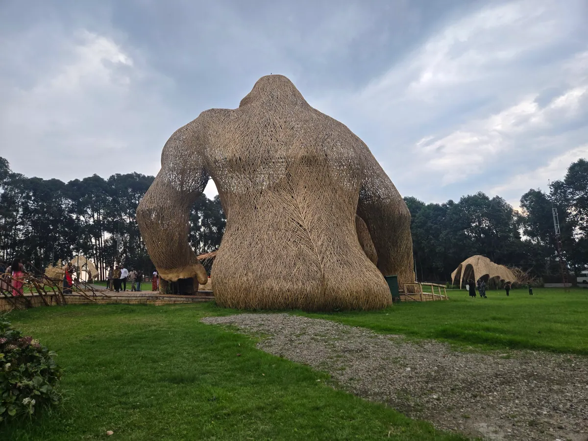The giant woven bamboo gorilla seen from behind, people walking beneath its arm