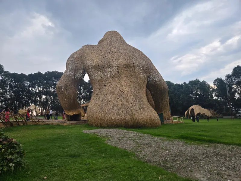 The giant woven bamboo gorilla seen from behind, people walking beneath its arm